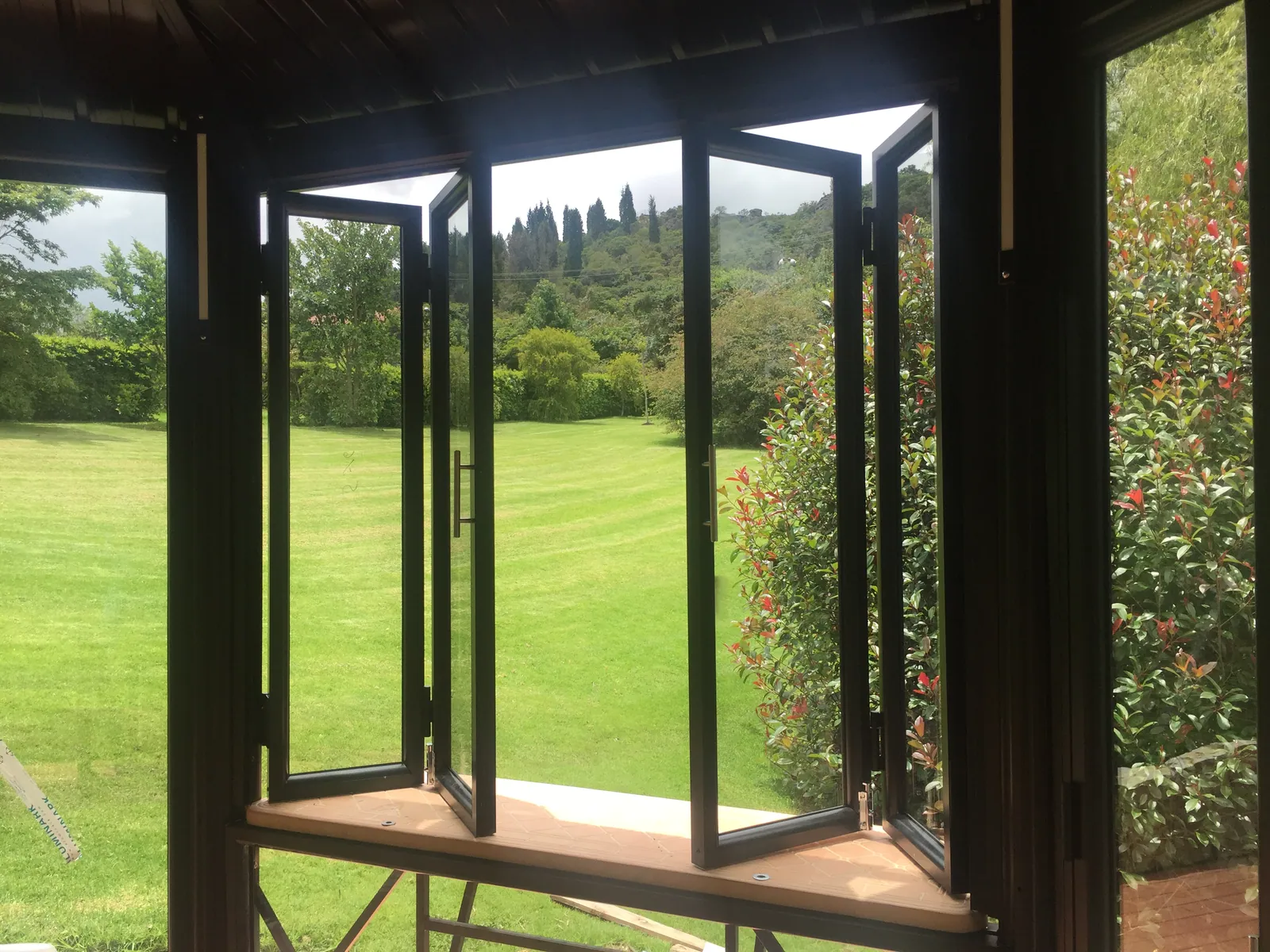 Cerramiento de terraza en aluminio con ventanas plegables abiertas al jardín, fabricado por ALUGANT