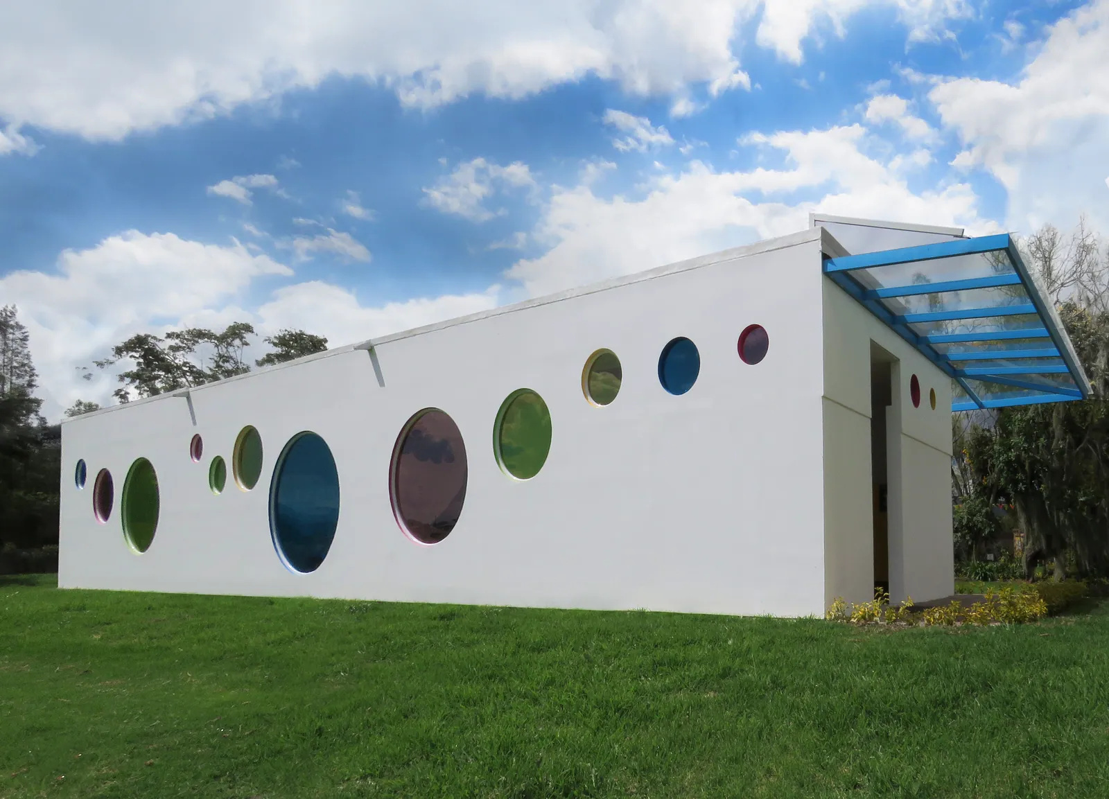 Gimnasio Infantil Las Villas: Ventanería, puertas plegables, marquesina y ventanas circulares de color para un jardín infantil. Carpintería a medida en cada aula, con vidrios de seguridad y herrajes protegidos.