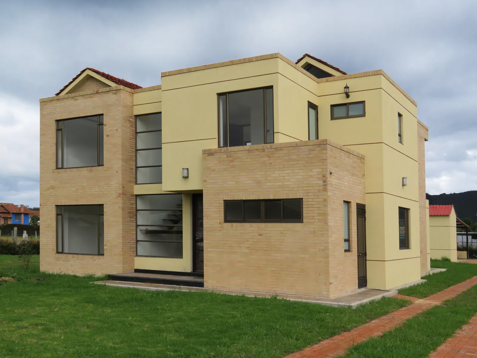 Vivienda Beltrán: Ventanería de piso a techo en una casa de volúmenes limpios. Ventanas fijas de gran formato, corredizas hacia el jardín y esquinas resueltas sin columna intermedia.